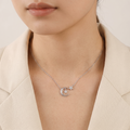 A close-up of a model wearing a delicate silver necklace with a crescent moon and star pendant, styled with a beige blazer.