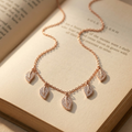 Rose gold leaf pendant necklace with pavÃ©-set clear stones, displayed on an open vintage book.